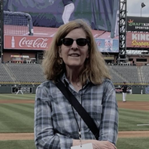 A photo of Renee Dechert standing in front of the Coors Field scoreboard during batting practice.